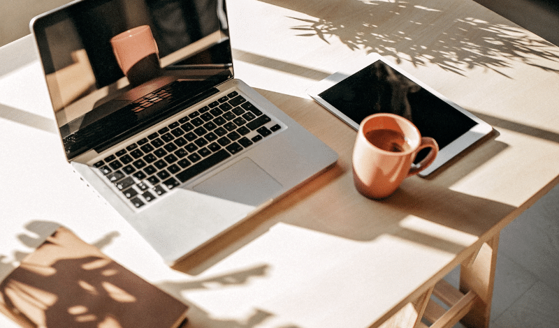 Ist ein Setup für Remote-Work auf der Terrasse mit Laptop, Tablet und einer Tasse Kaffee zu sehen.